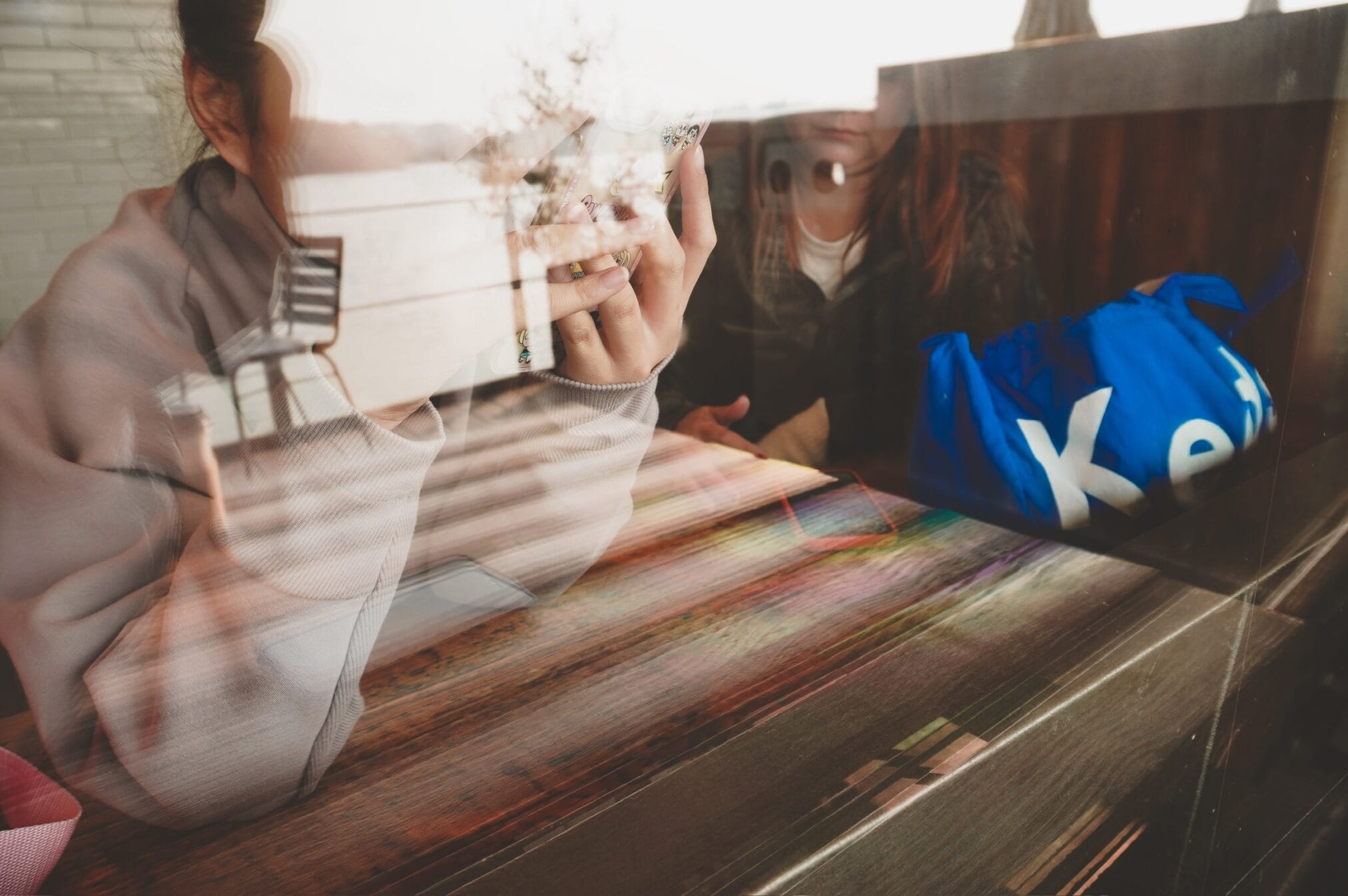 ผู้หญิงนั่งในร้านกาแฟ มองออกไปนอกหน้าต่าง มีถุงสีน้ำเงินวางอยู่บนโต๊ะ