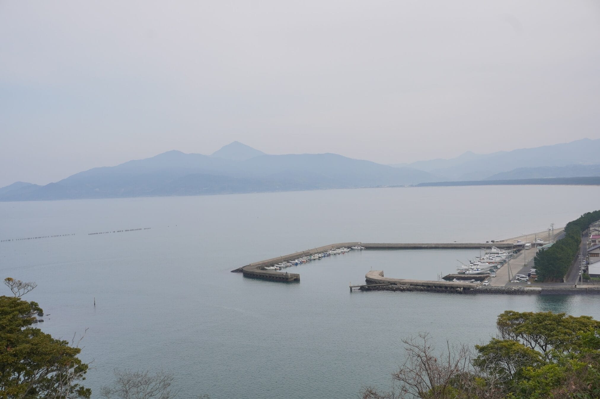 ท่าจอดเรือเล็กในภูมิภาคคิวชู มีเรือจอดเรียงราย วิวภูเขาอยู่ไกลๆ
