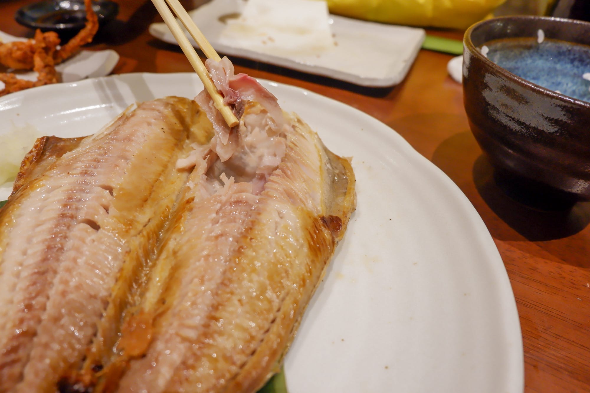 ปลาทั้งตัวย่างบนจานสีขาว พร้อมตะเกียบกำลังคีบเนื้อปลา