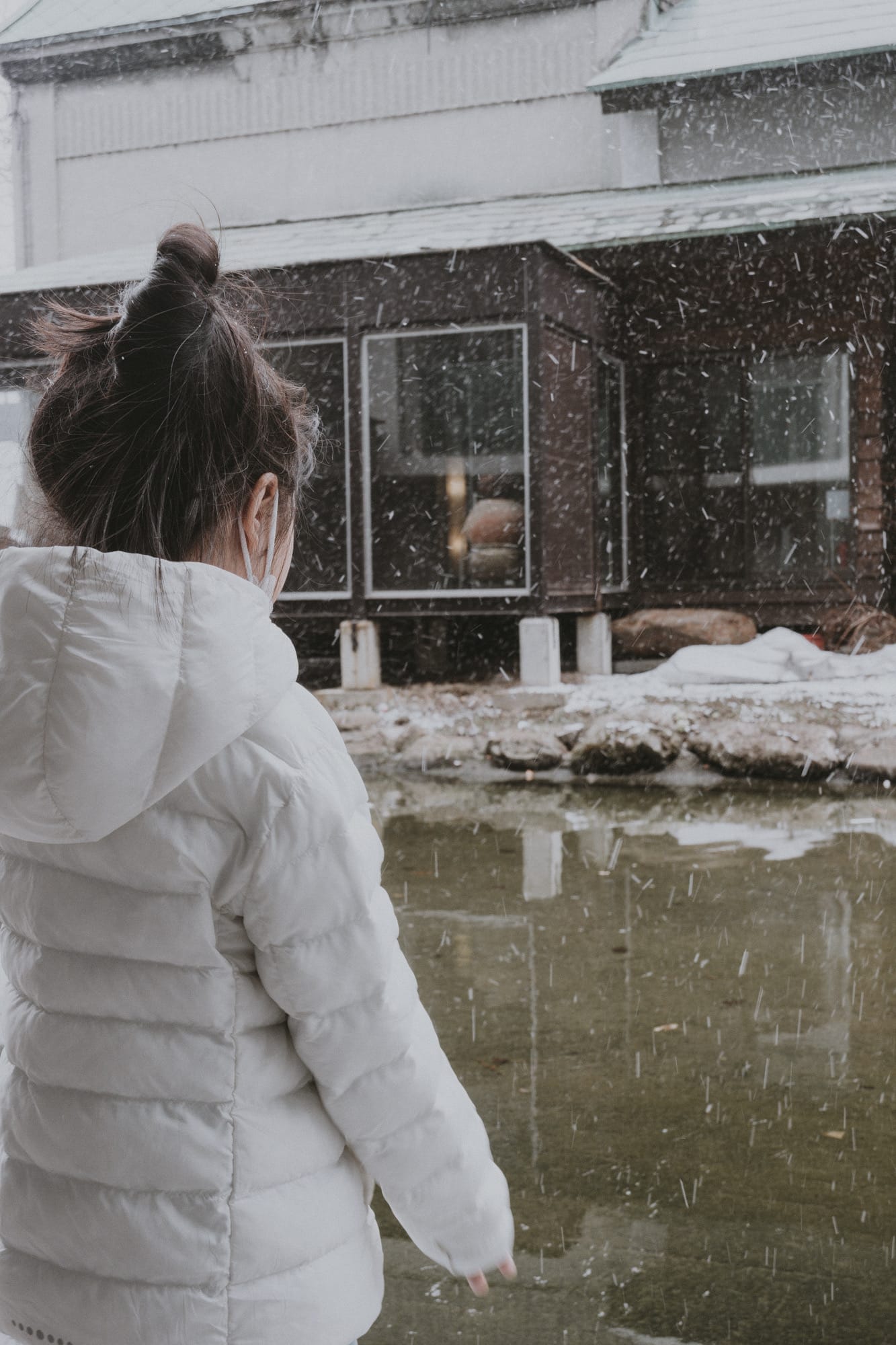 เด็กหญิงใส่เสื้อโค้ทสีขาว มองดูหิมะตกที่ฮอกไกโด