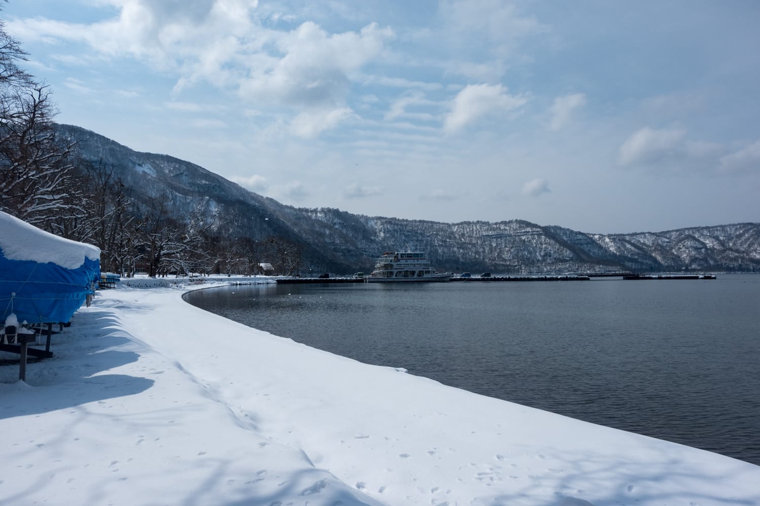 หาดหิมะริมทะเลสาบ เรือเทียบท่า ภูเขาหิมะและท้องฟ้าครึ้ม