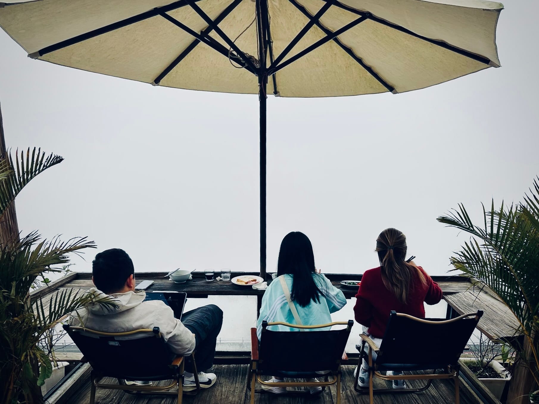 คนสามคนนั่งทานอาหารใต้ร่มกันแดดบนระเบียง