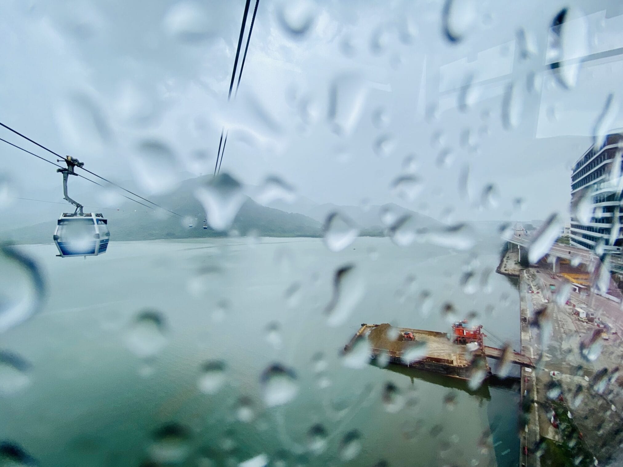 กระเช้าลอยฟ้าเหนือทะเลฮ่องกงในวันที่ฝนตก มองเห็นวิวเกาะและท่าเรือ