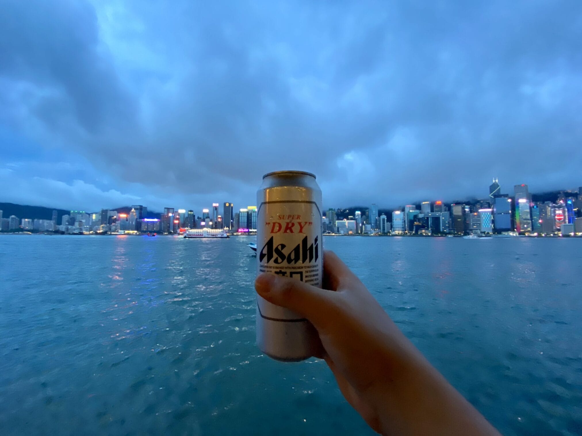มือถือกระป๋องเบียร์ Asahi ดื่มชมวิวเมืองฮ่องกงริมอ่าว Asahi beer can held with Hong Kong harbor cityscape background