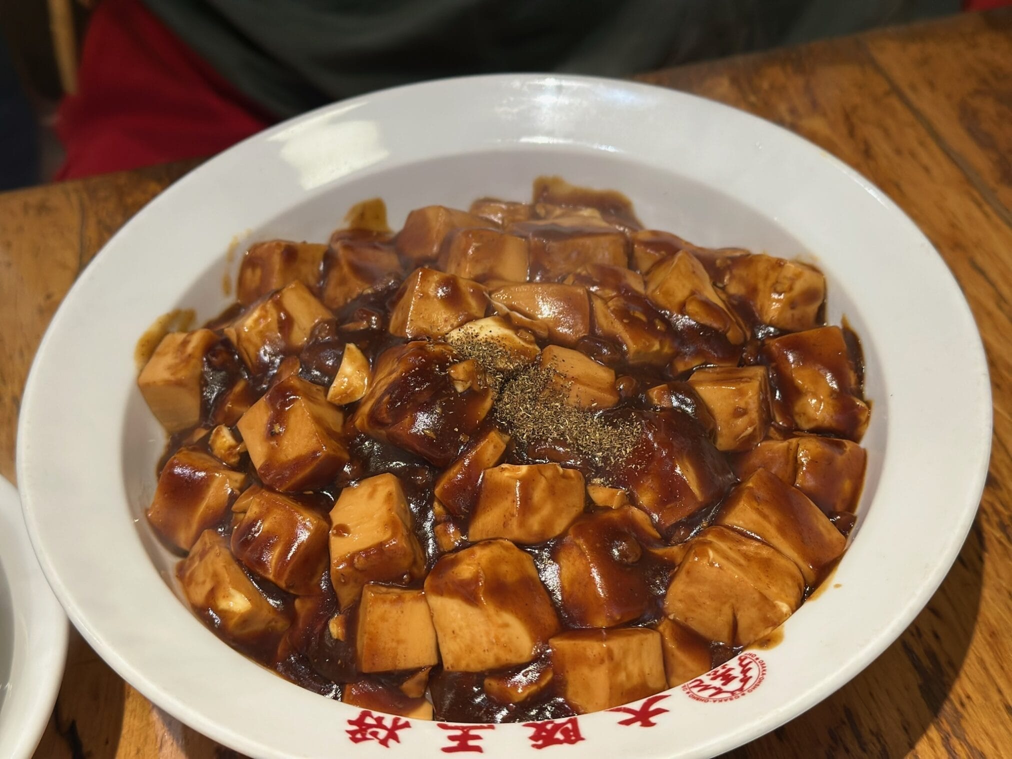 เต้าหู้มาโปในจานสีขาว มีตัวอักษรจีนสีแดงด้านล่าง