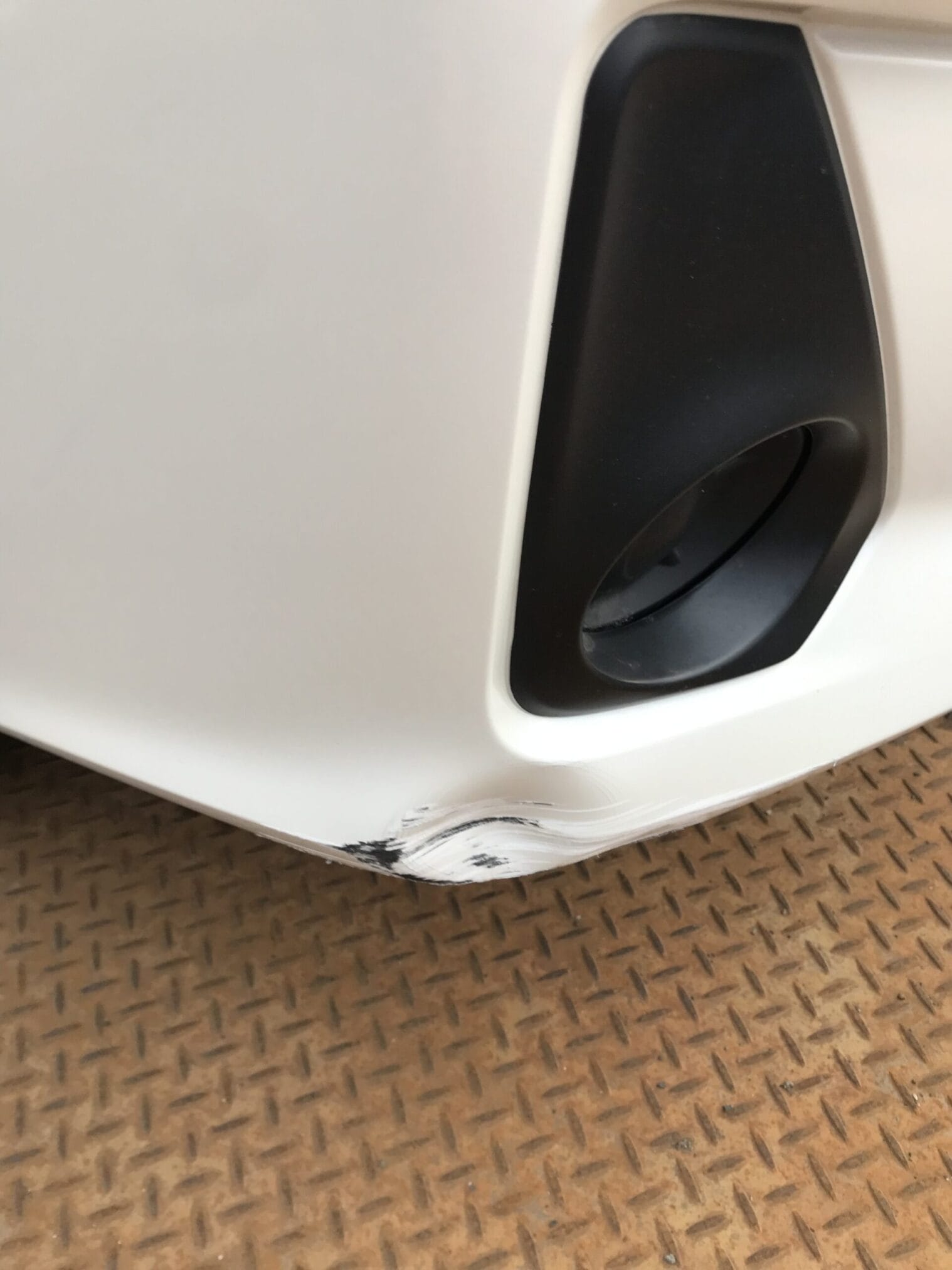 รอยขีดข่วนสีดำบนกันชนหน้ารถสีขาว ใกล้ไฟตัดหมอก