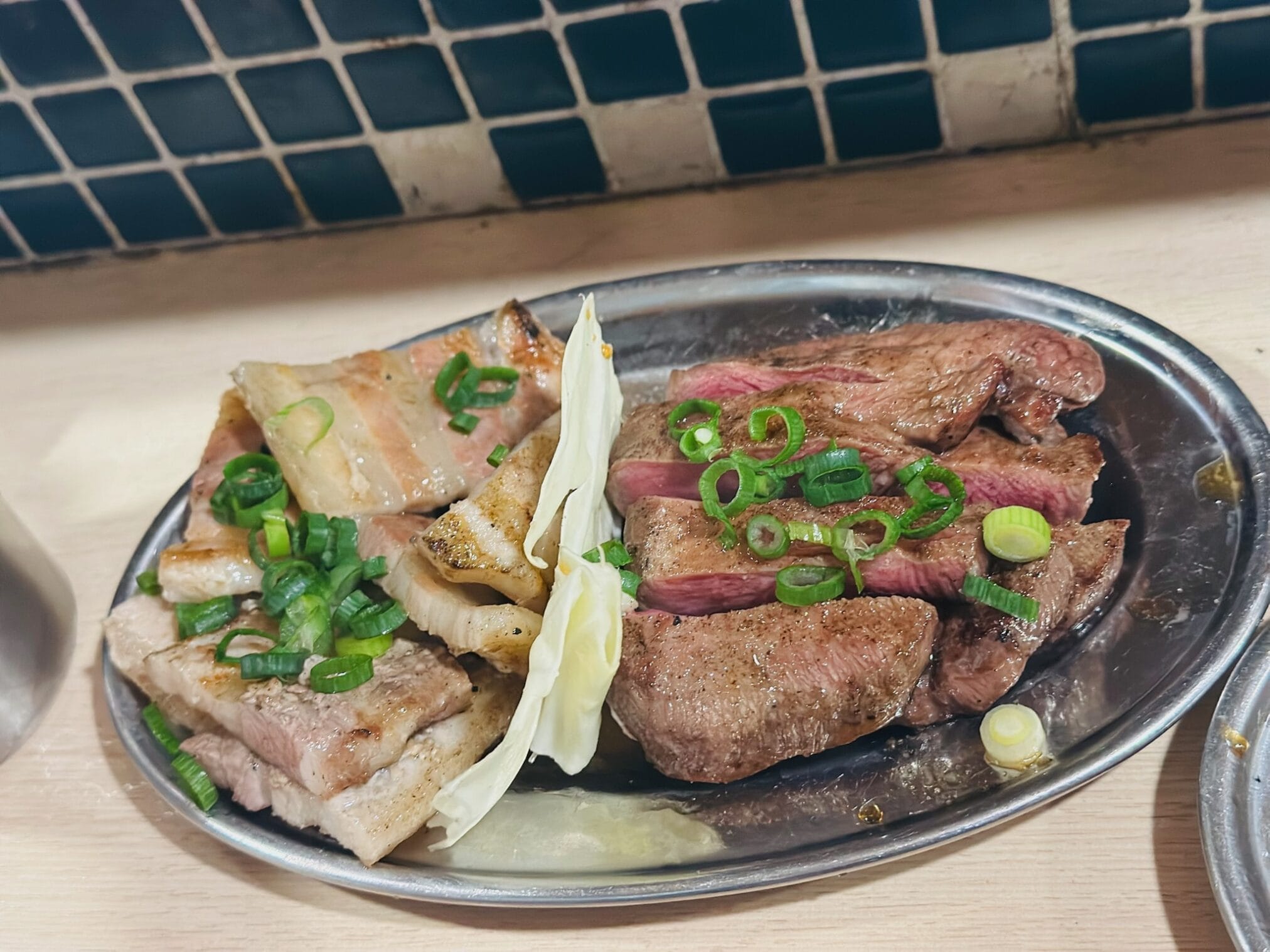 เนื้อย่างและหมูย่างโรยหน้าด้วยต้นหอมซอยบนจานโลหะในร้านอาหารที่ฟุกุโอกะ