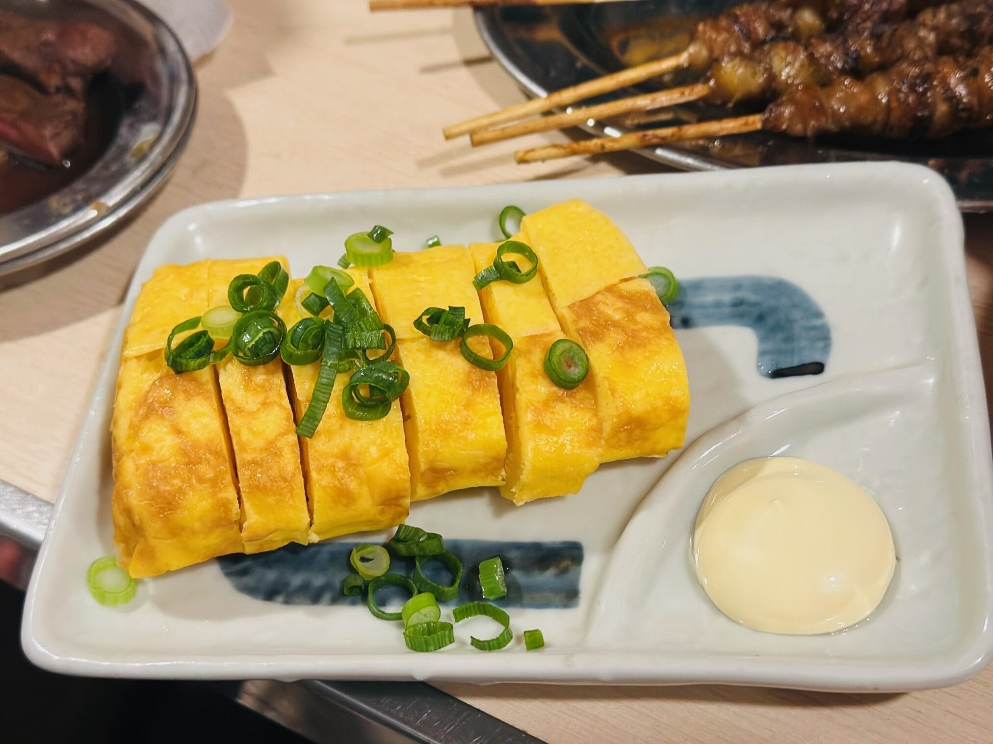 ไข่ม้วนญี่ปุ่นท็อปปิ้งต้นหอมบนจานสีขาว พร้อมมายองเนส ในทริปขับรถเที่ยวคิวชู