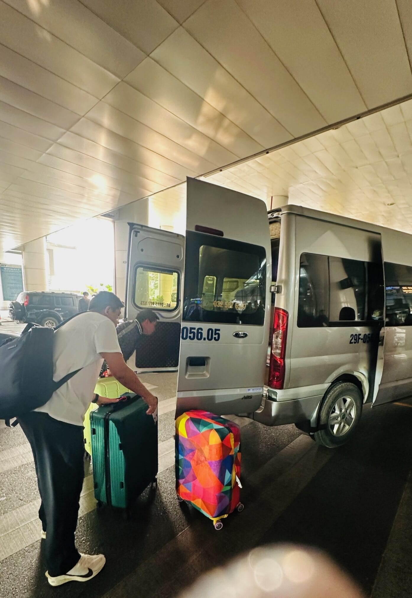 ผู้ชายกำลังยกกระเป๋าเดินทางสีสันสดใสขึ้นรถตู้ที่ฮานอย