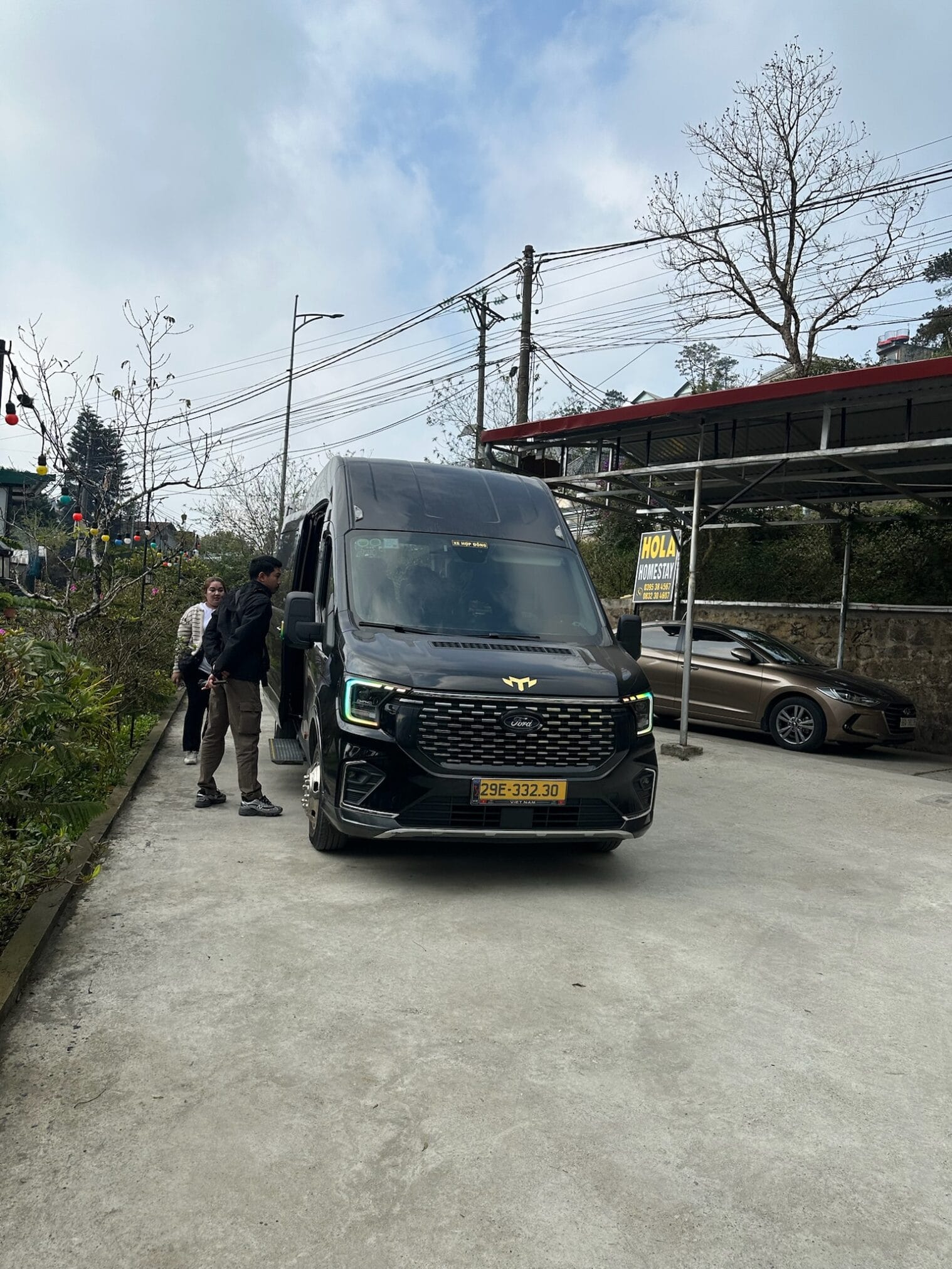 รถตู้สีดำจอดอยู่ด้านนอกโฮมสเตย์ "Hola Homestay" หมายเลขทะเบียนรถ 29E-332.30