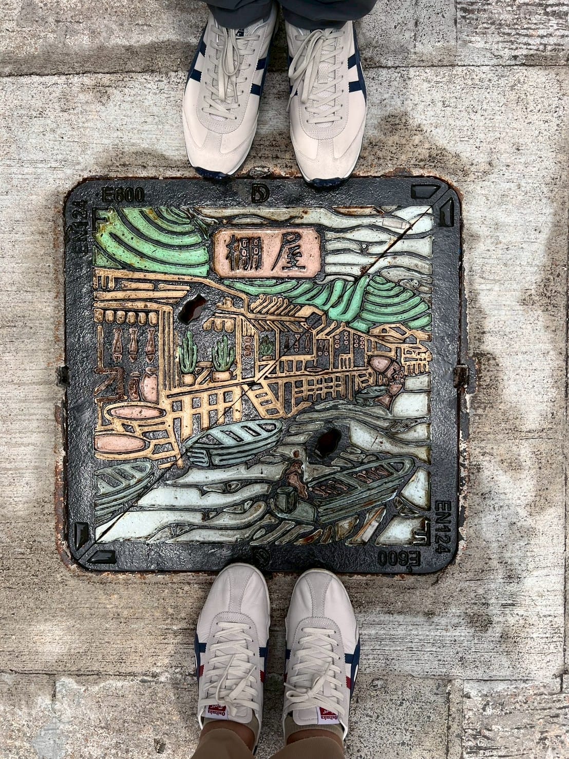 ถนนพร้อมฝาท่อเหล็กหล่อมีลายภาพเรือและบ้าน Shoes on decorated manhole cover with boat and house design