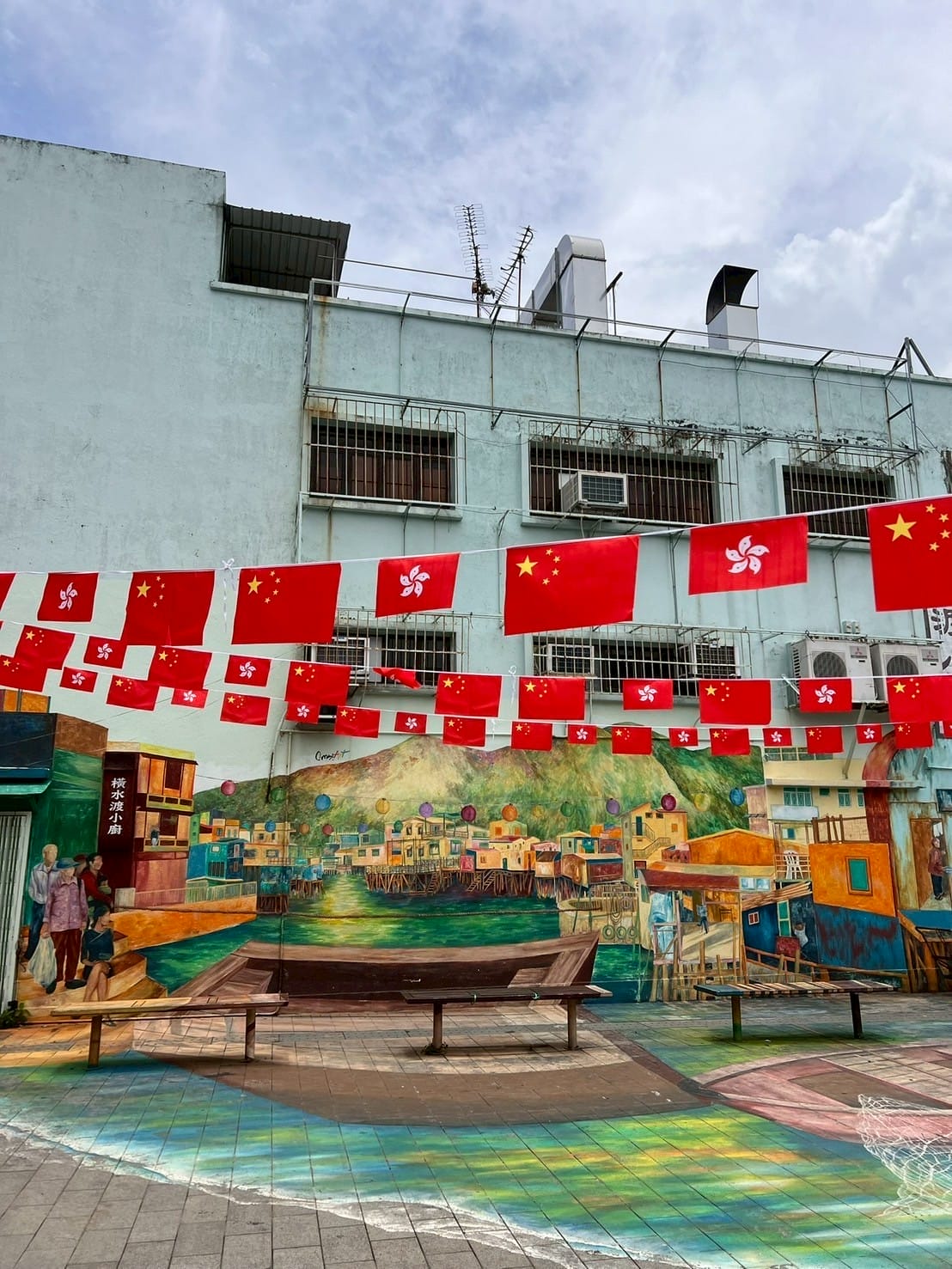 ธงชาติฮ่องกงและจีนแขวนประดับเหนือผนังภาพวาดเมืองริมทะเล Hong Kong and China flags hanging above colorful seaside mural