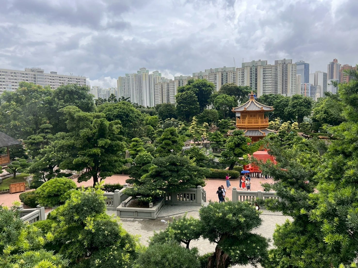 สวนญี่ปุ่นเขียวขจีมีศาลาไม้และสะพานแดง ท่ามกลางตึกสูงในเมือง Japanese garden with wooden pavilion and red bridge surrounded by green trees and city skyscrapers
